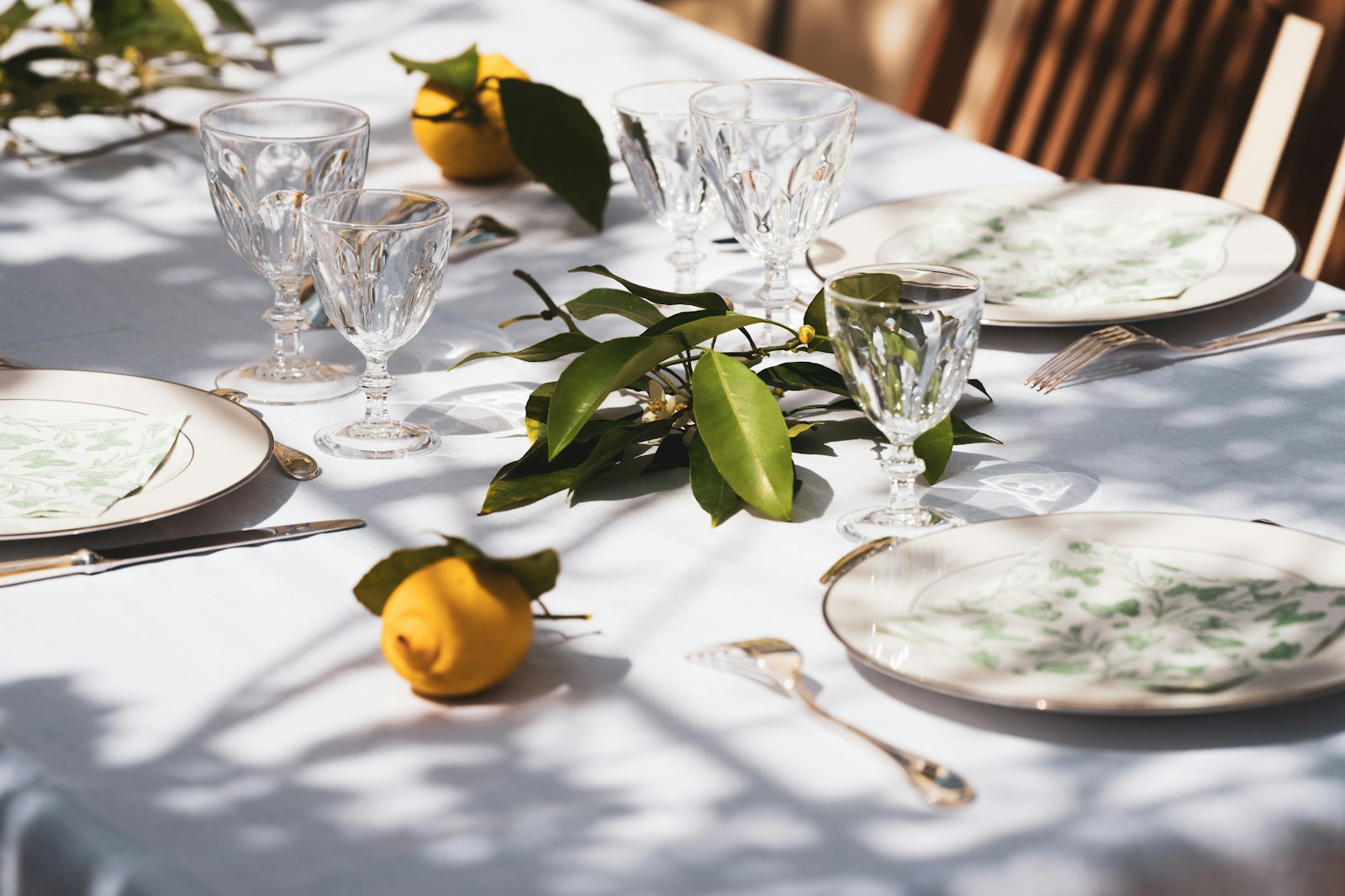A table set with plates, crystal glasses and lemons in sunlight