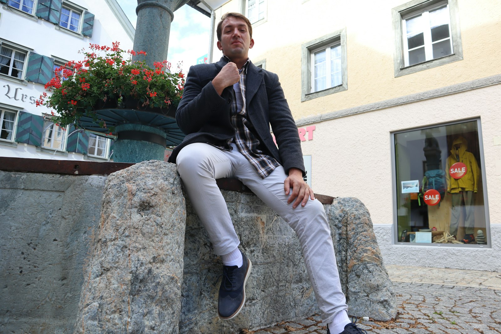 Man in an elegant smart-casual outfit seated on a stone wall in the city — men's pleated trousers guide