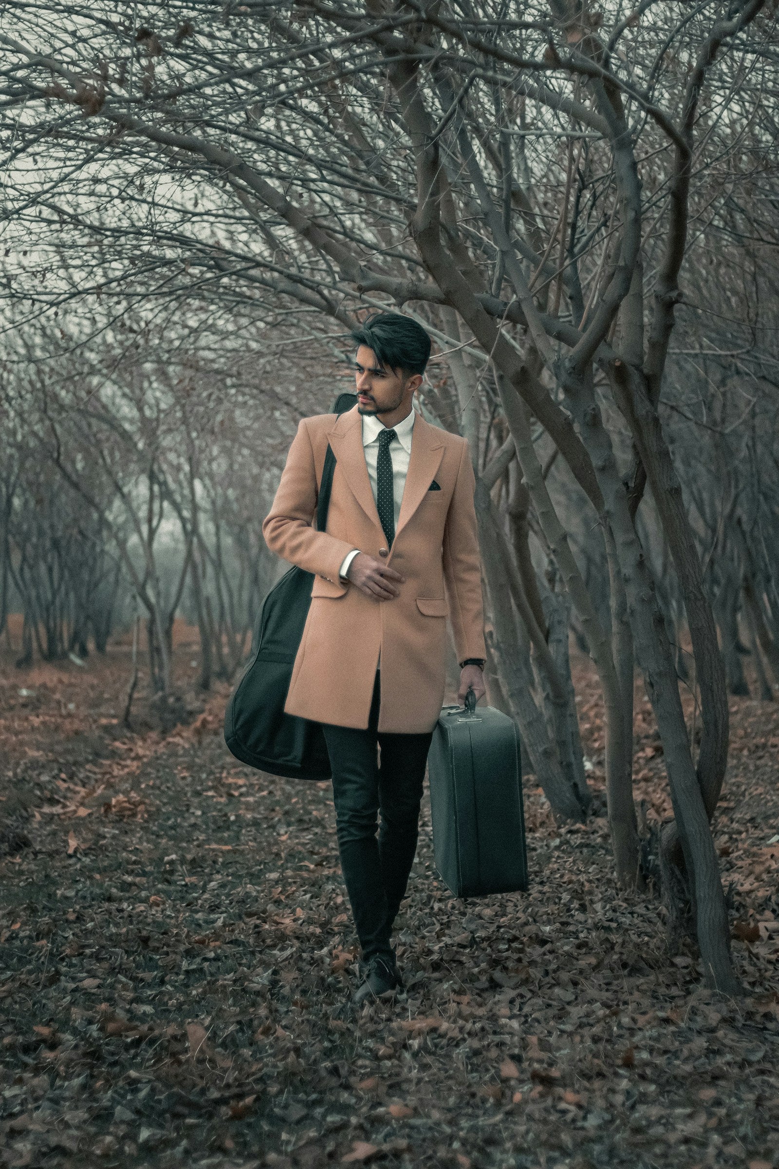 Man in a camel overcoat walking through autumn woodland