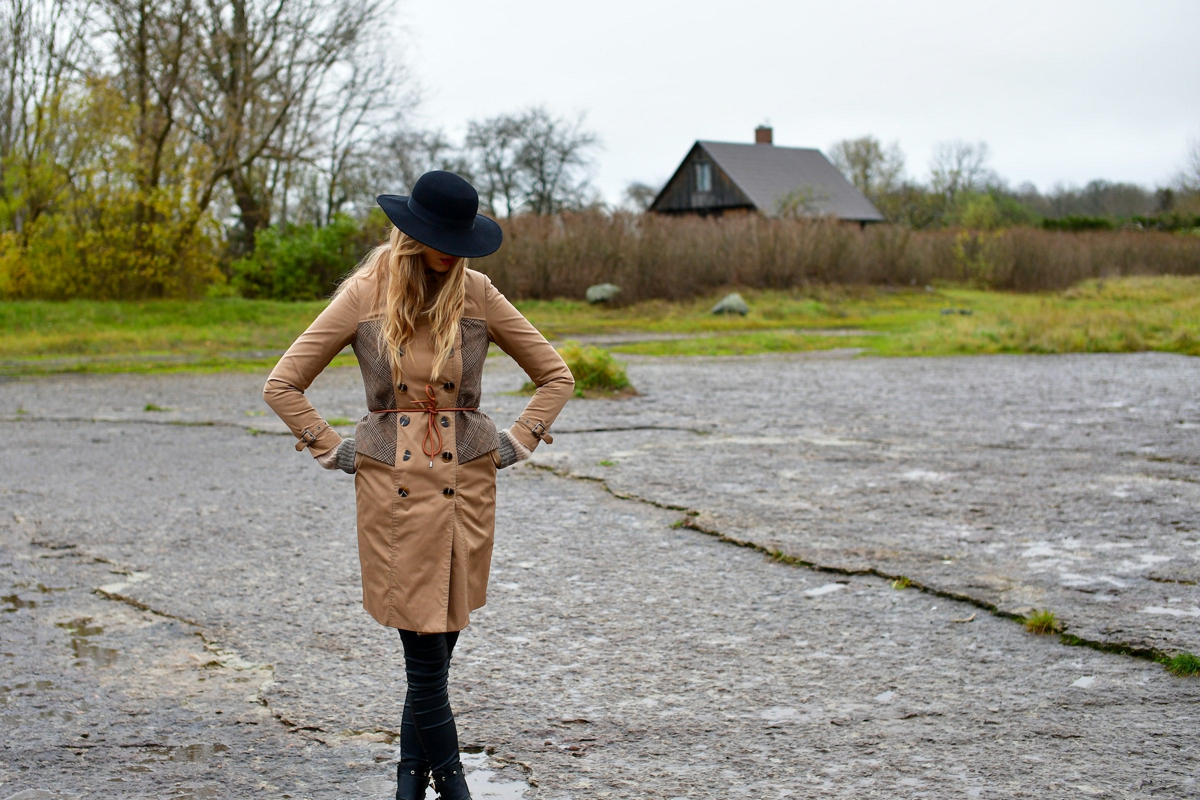 Woman in a trench coat and hat walking by a river in autumn